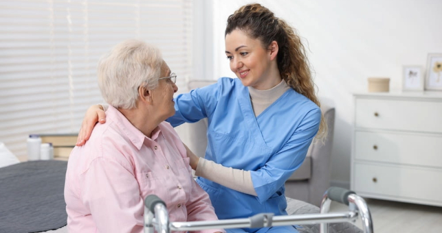 Care worker supporting senior woman in room