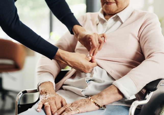 Nurse dressing old woman in wheelchair